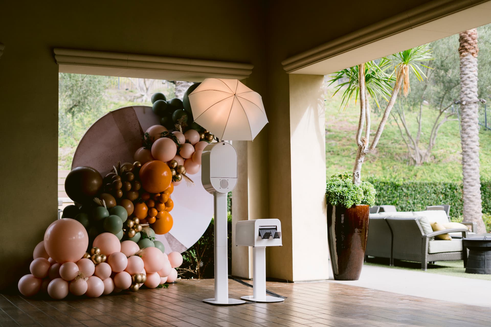 Memento photo booth set up beside a blush and olive balloon arch